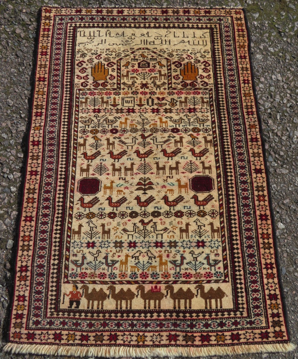 Hand-knotted wool Baluch prayer rug with a cream field featuring stylized camels, birds, hand symbols, and a mihrab top border.