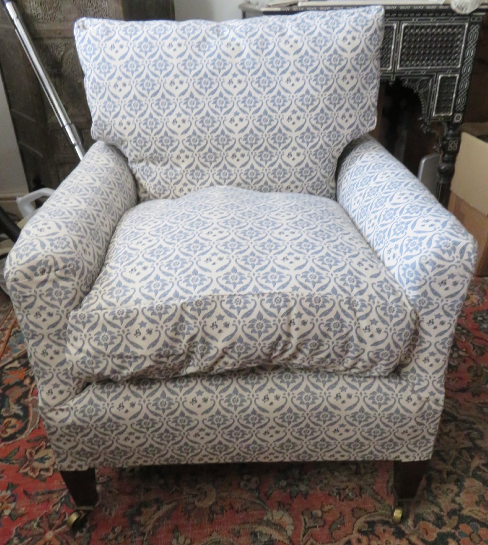 A deeply cushioned upholstered armchair featuring blue and cream patterned fabric, padded arms, and dark tapered wooden legs on brass castors.