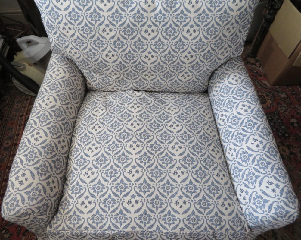 A deeply cushioned upholstered armchair featuring blue and cream patterned fabric, padded arms, and dark tapered wooden legs on brass castors. View III