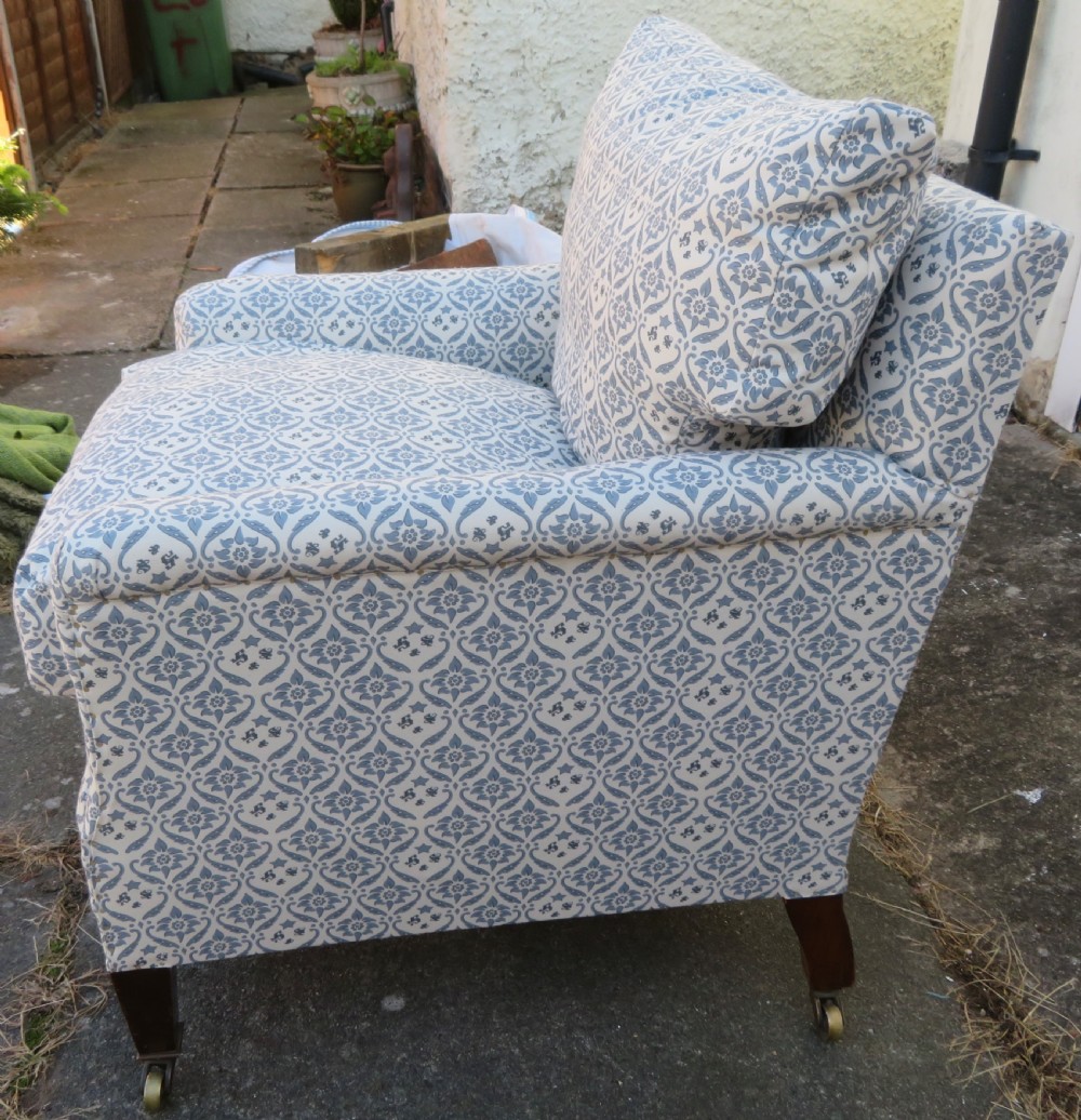 A deeply cushioned upholstered armchair featuring blue and cream patterned fabric, padded arms, and dark tapered wooden legs on brass castors. View V