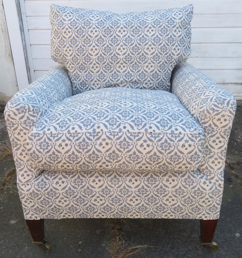 A deeply cushioned upholstered armchair featuring blue and cream patterned fabric, padded arms, and dark tapered wooden legs on brass castors. View VI