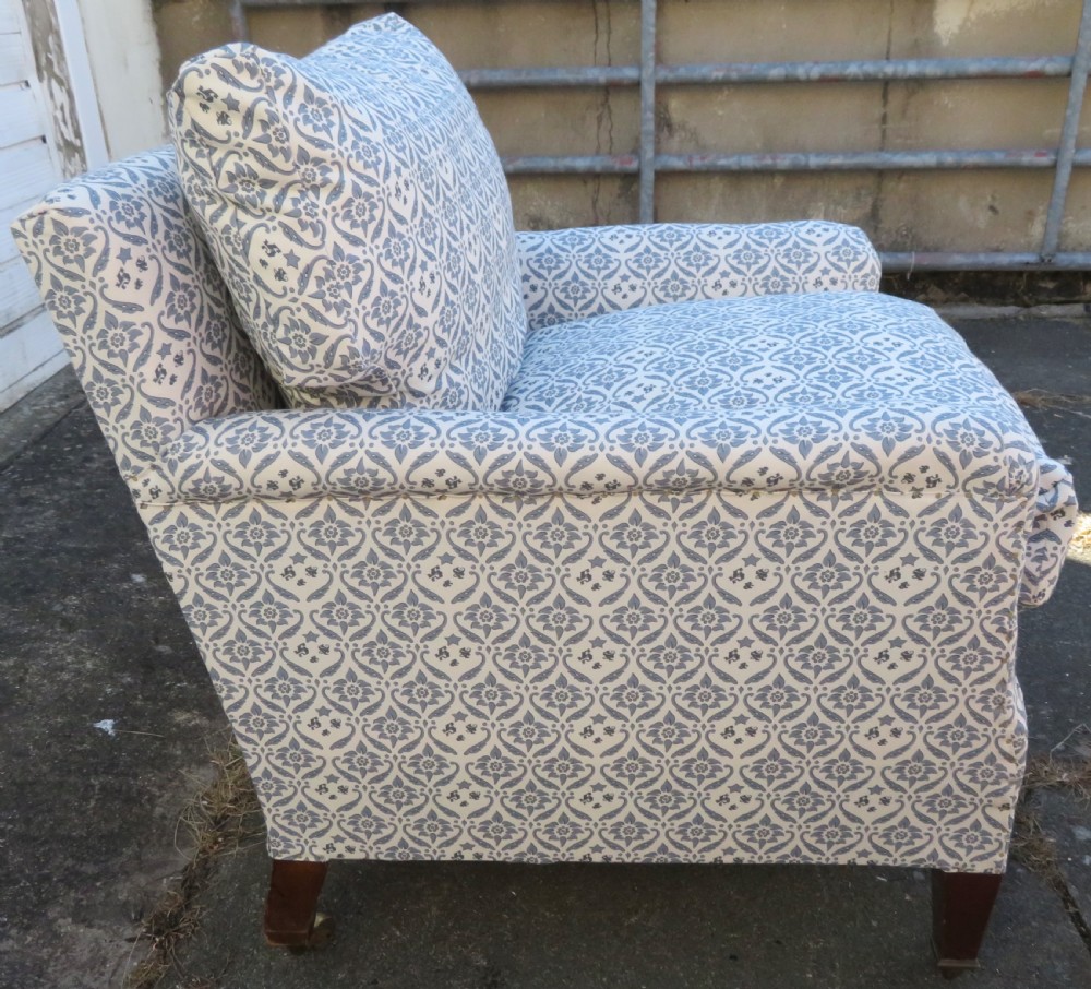 A deeply cushioned upholstered armchair featuring blue and cream patterned fabric, padded arms, and dark tapered wooden legs on brass castors. View VII
