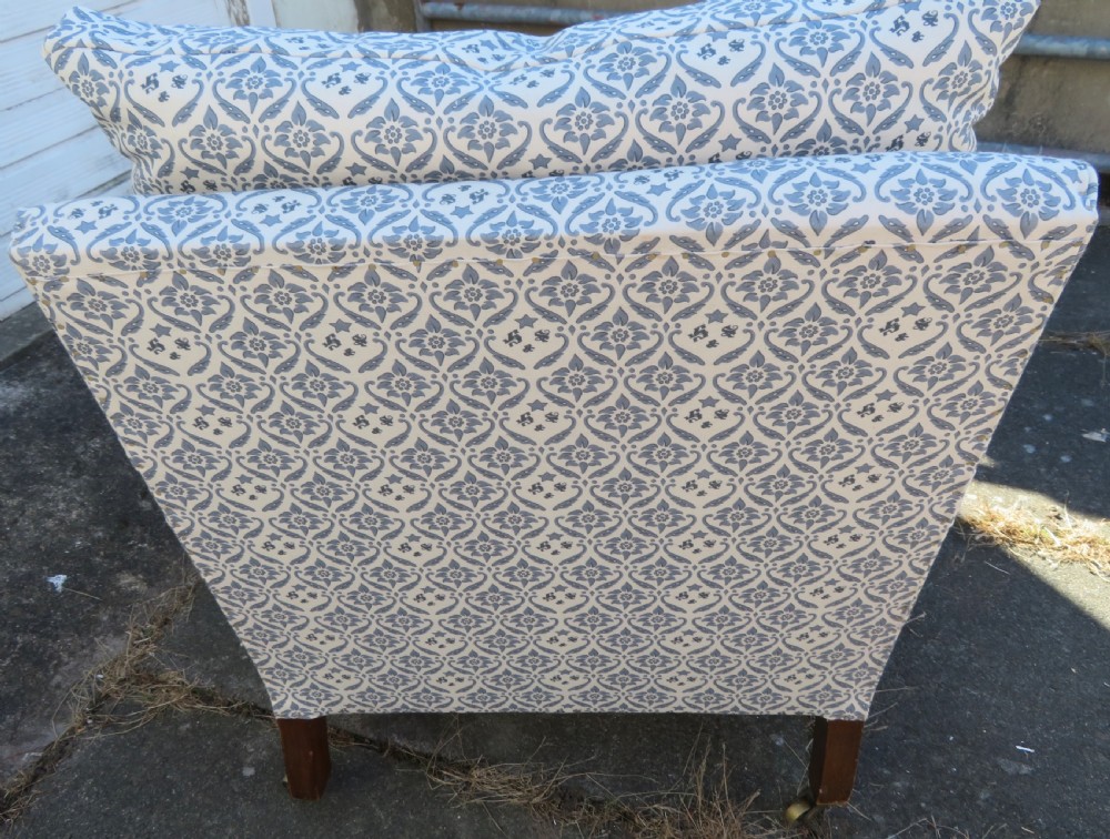 A deeply cushioned upholstered armchair featuring blue and cream patterned fabric, padded arms, and dark tapered wooden legs on brass castors. View X