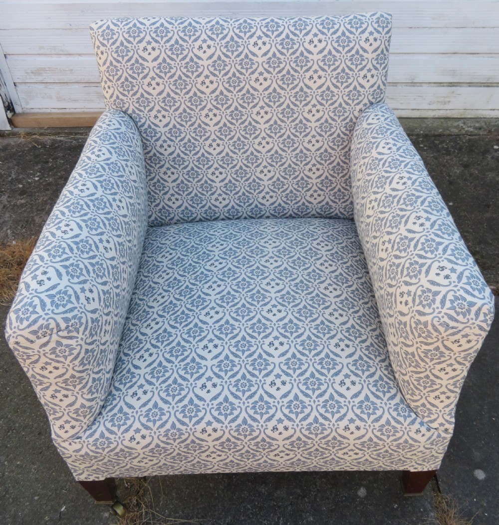 A deeply cushioned upholstered armchair featuring blue and cream patterned fabric, padded arms, and dark tapered wooden legs on brass castors. View XI