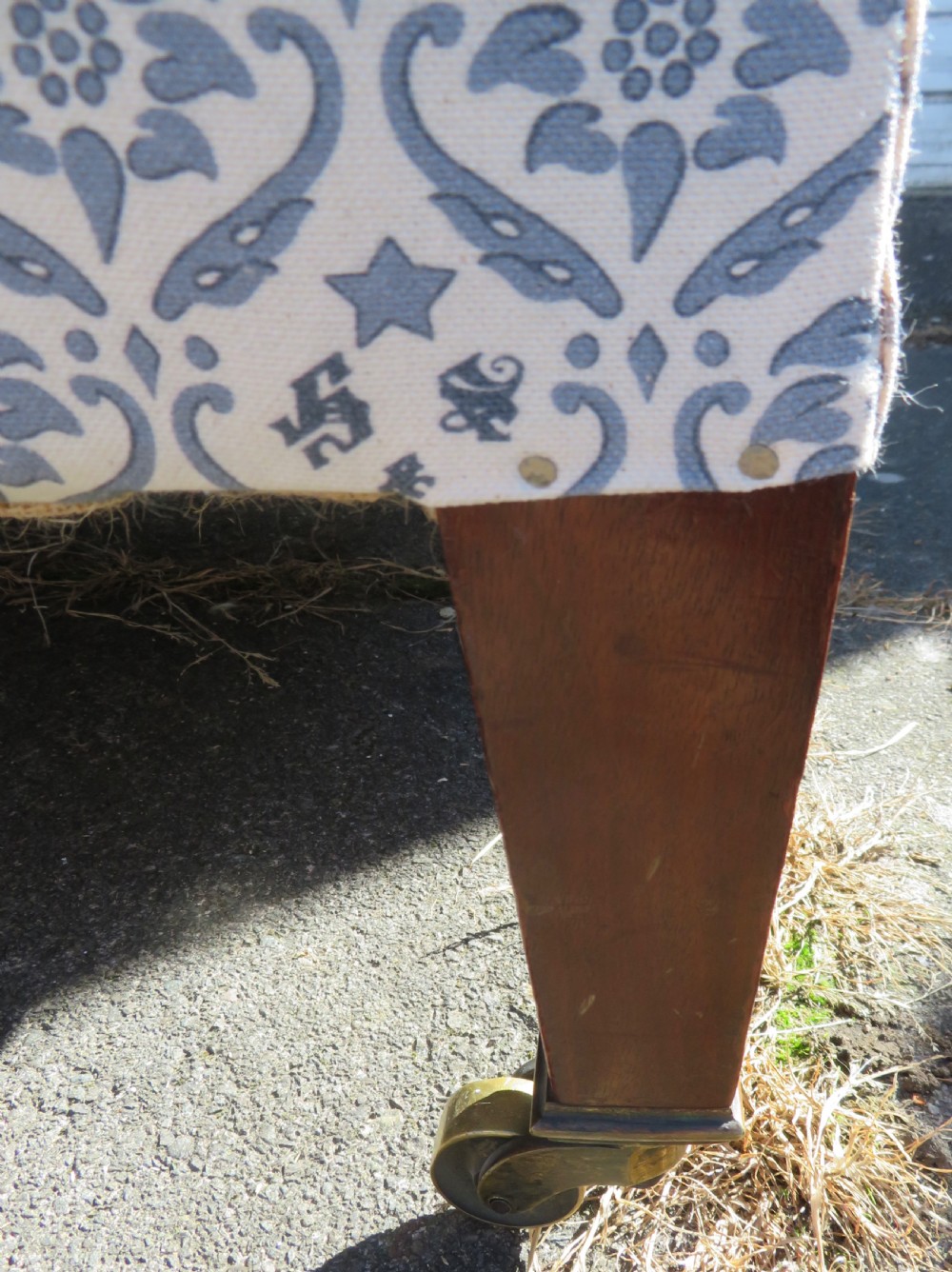 A deeply cushioned upholstered armchair featuring blue and cream patterned fabric, padded arms, and dark tapered wooden legs on brass castors. View XXI