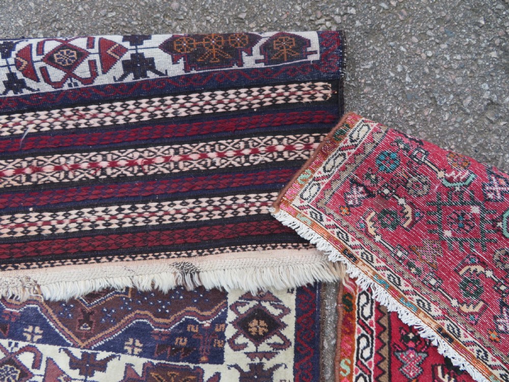 A pair of hand-woven tribal wool rugs featuring geometric medallions in tones of red, blue, brown, and cream with fringed edges. View X