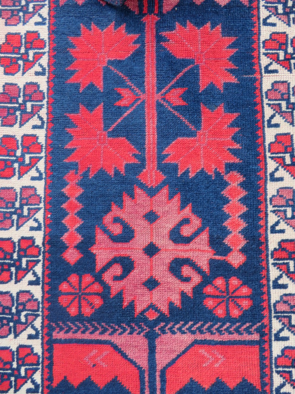 A long, narrow hand-knotted Turkish Yagjibedir runner rug featuring geometric tribal motifs in deep red against a dark navy blue background with a patterned ivory border. View II
