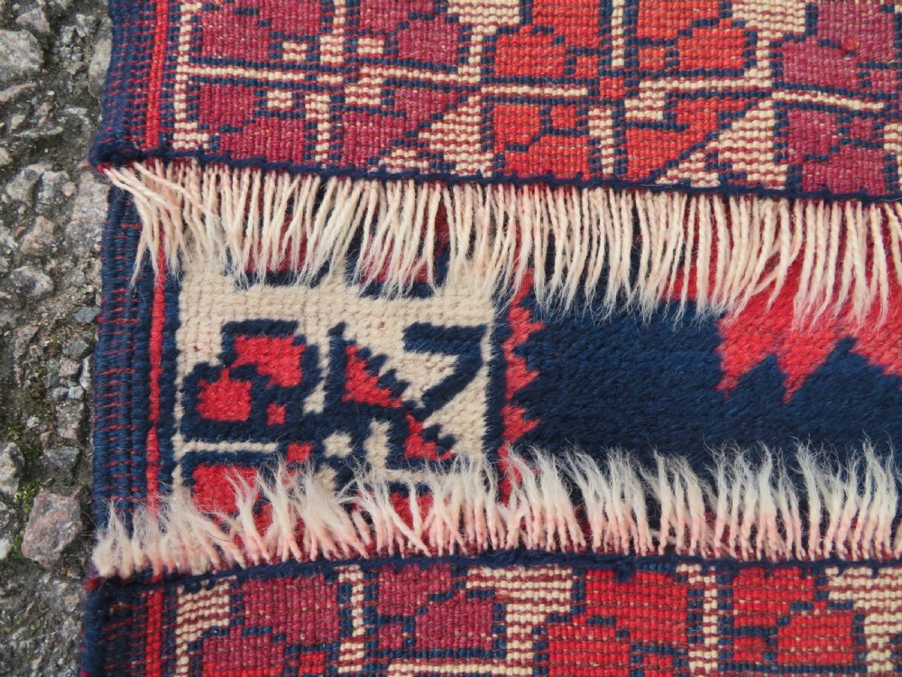 A long, narrow hand-knotted Turkish Yagjibedir runner rug featuring geometric tribal motifs in deep red against a dark navy blue background with a patterned ivory border. View IX