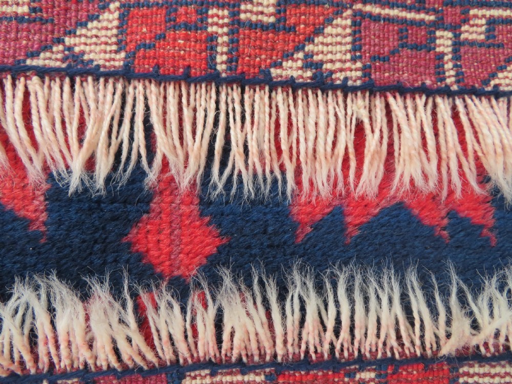 A long, narrow hand-knotted Turkish Yagjibedir runner rug featuring geometric tribal motifs in deep red against a dark navy blue background with a patterned ivory border. View X