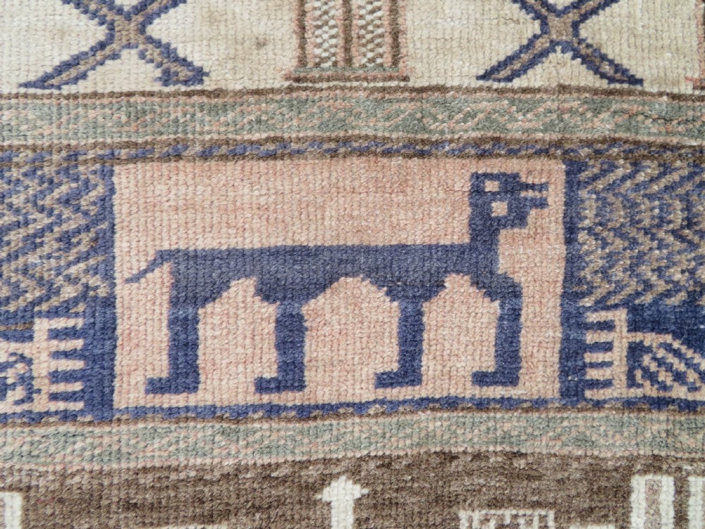 A hand-knotted Afghan wool rug featuring panelled sections with stylized animal motifs and geometric borders in terracotta, beige, brown, and navy blue hues. View VI