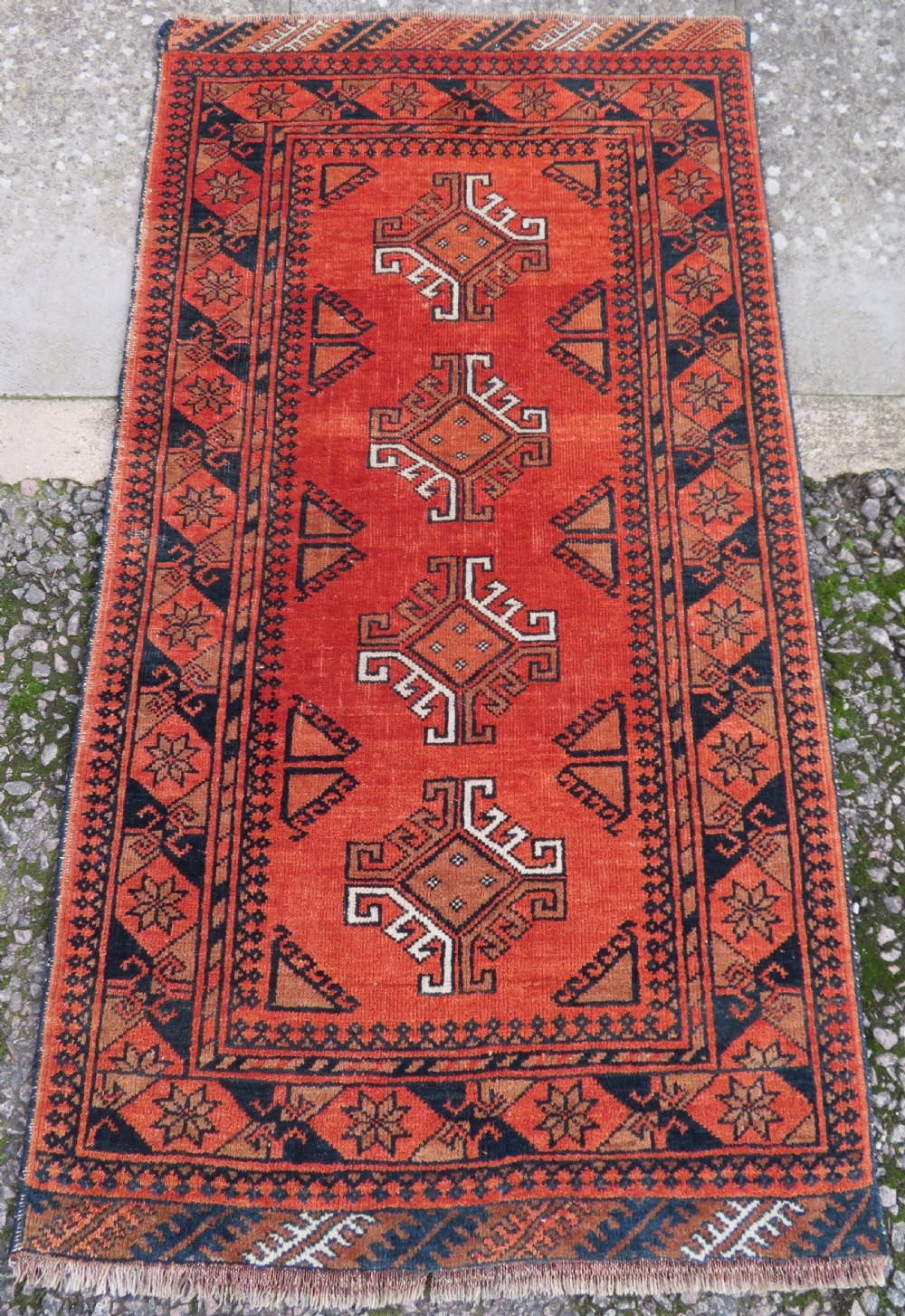 A hand-knotted Afghan wool rug featuring a rust-red field decorated with four diamond latch-hook medallions and geometric borders.