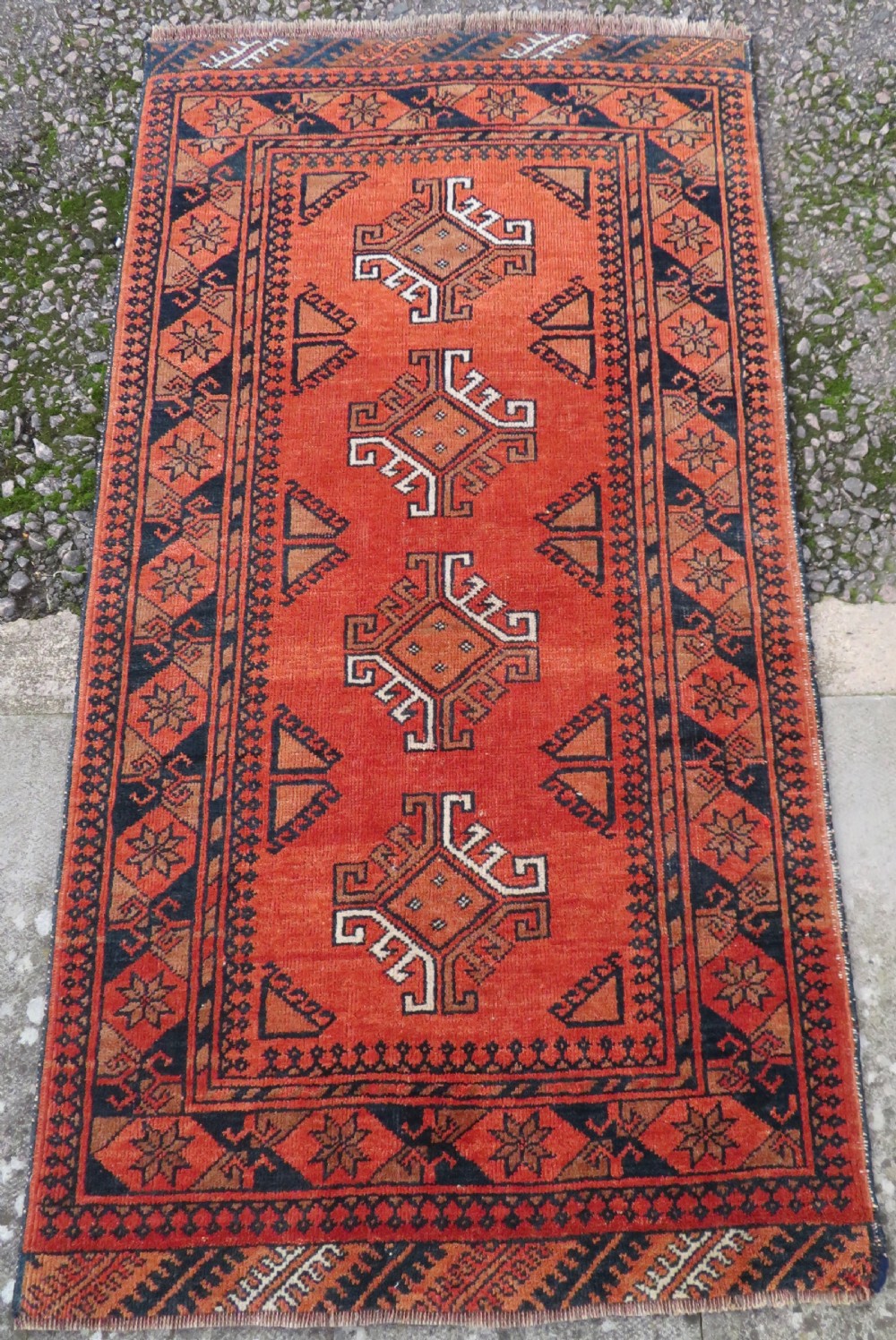 A hand-knotted Afghan wool rug featuring a rust-red field decorated with four diamond latch-hook medallions and geometric borders. View II