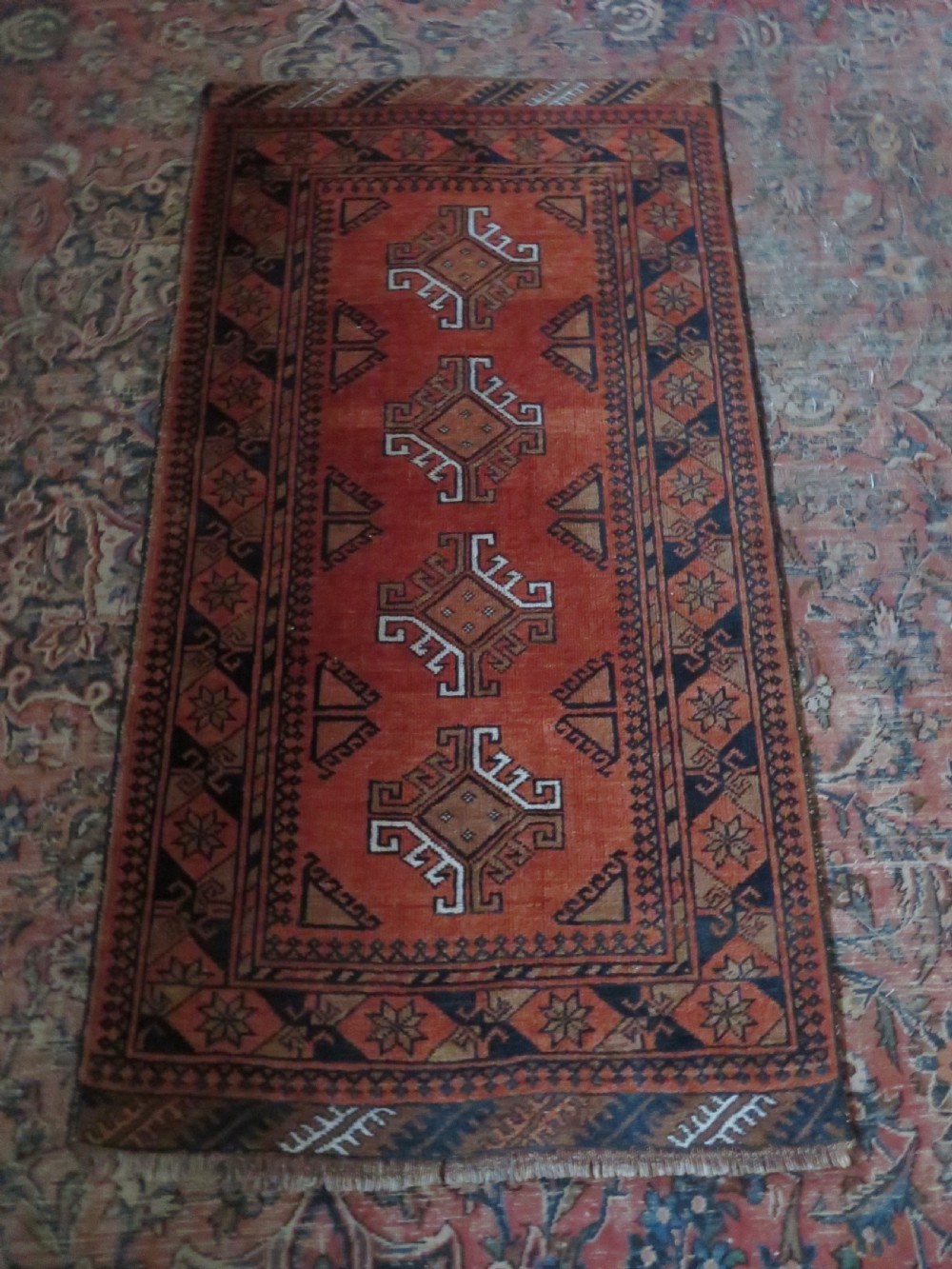 A hand-knotted Afghan wool rug featuring a rust-red field decorated with four diamond latch-hook medallions and geometric borders. View III