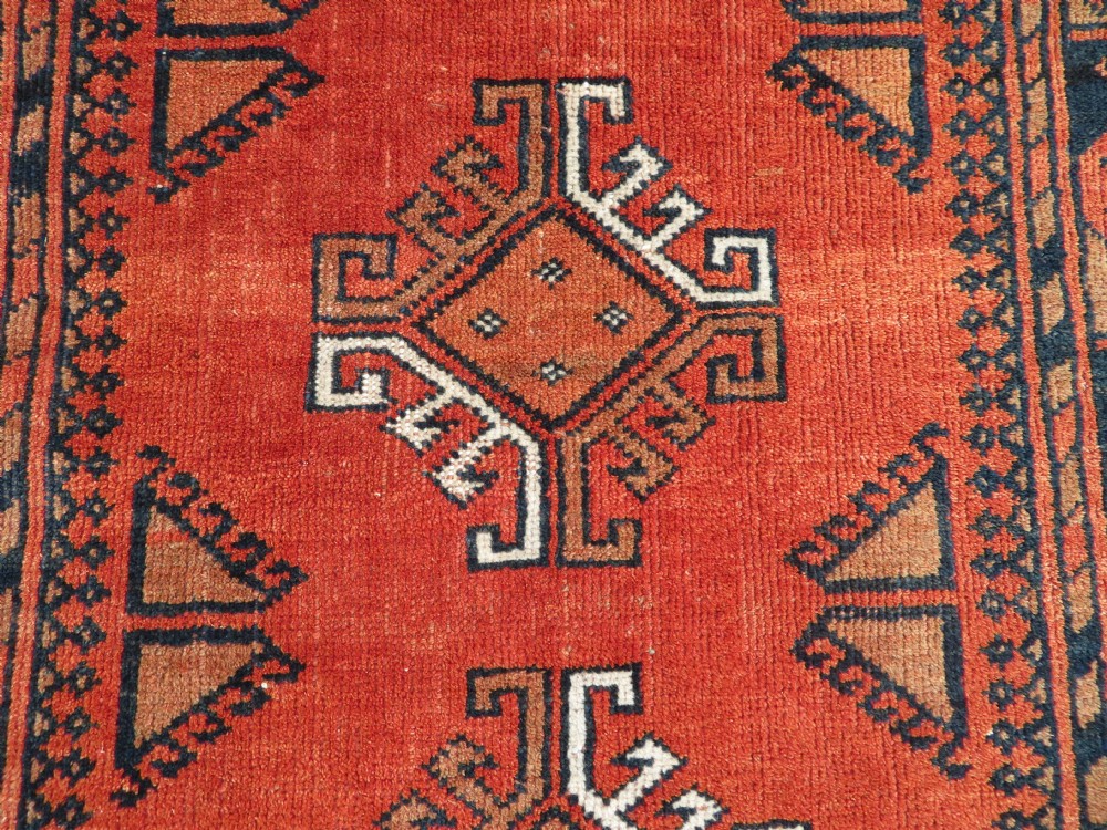 A hand-knotted Afghan wool rug featuring a rust-red field decorated with four diamond latch-hook medallions and geometric borders. View V