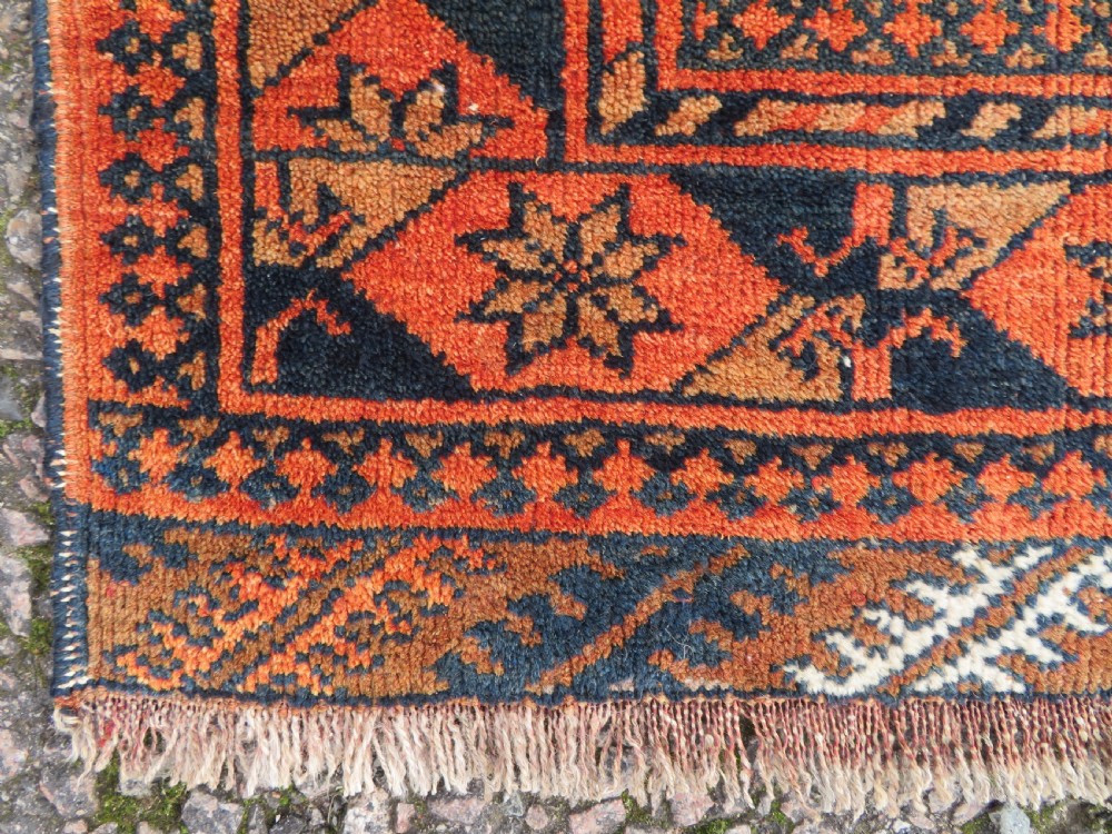 A hand-knotted Afghan wool rug featuring a rust-red field decorated with four diamond latch-hook medallions and geometric borders. View VIII