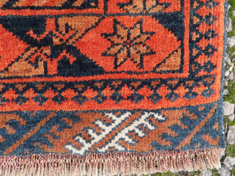 A hand-knotted Afghan wool rug featuring a rust-red field decorated with four diamond latch-hook medallions and geometric borders. View IX