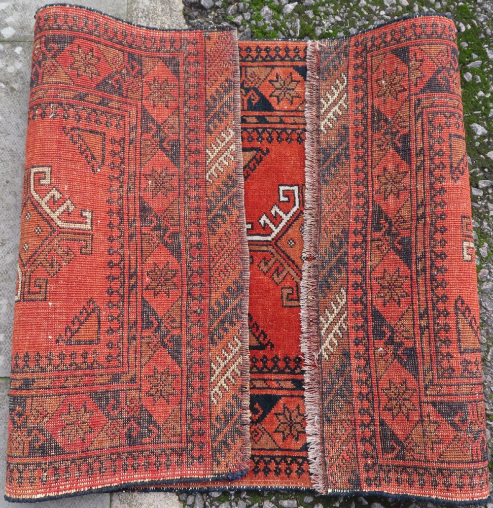 A hand-knotted Afghan wool rug featuring a rust-red field decorated with four diamond latch-hook medallions and geometric borders. View XII