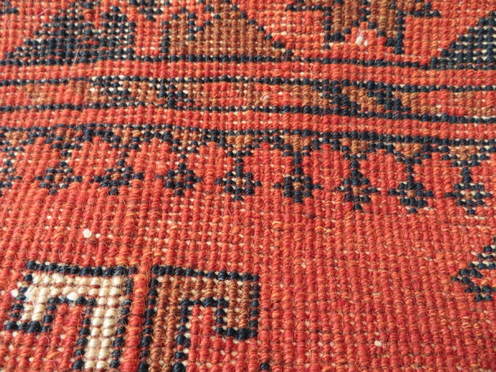 A hand-knotted Afghan wool rug featuring a rust-red field decorated with four diamond latch-hook medallions and geometric borders. View XIV