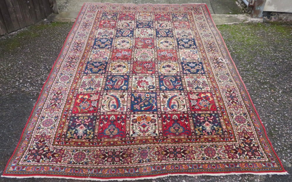 A large hand-knotted Persian Qum carpet with a square compartment panel design featuring floral and boteh motifs in red, blue, and cream enclosed by multi-band borders.