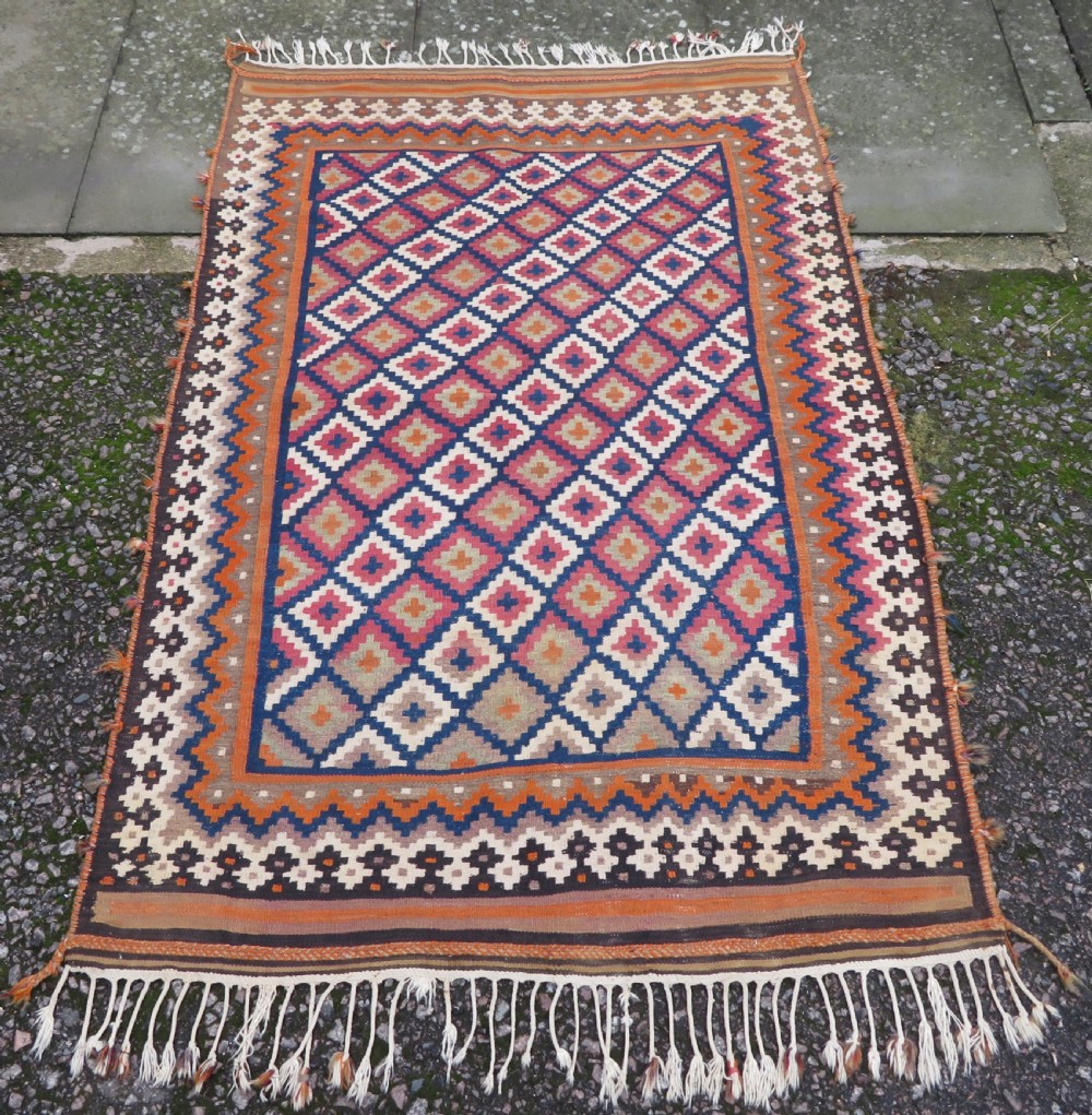A handwoven Qashqai kilim rug featuring a geometric diamond lattice pattern in terracotta, navy blue, red, and cream with fringed ends.