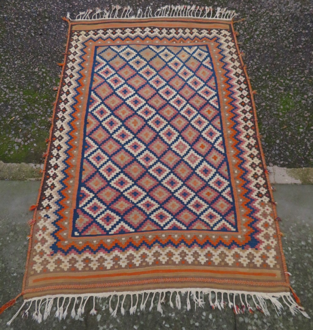 A handwoven Qashqai kilim rug featuring a geometric diamond lattice pattern in terracotta, navy blue, red, and cream with fringed ends. View II
