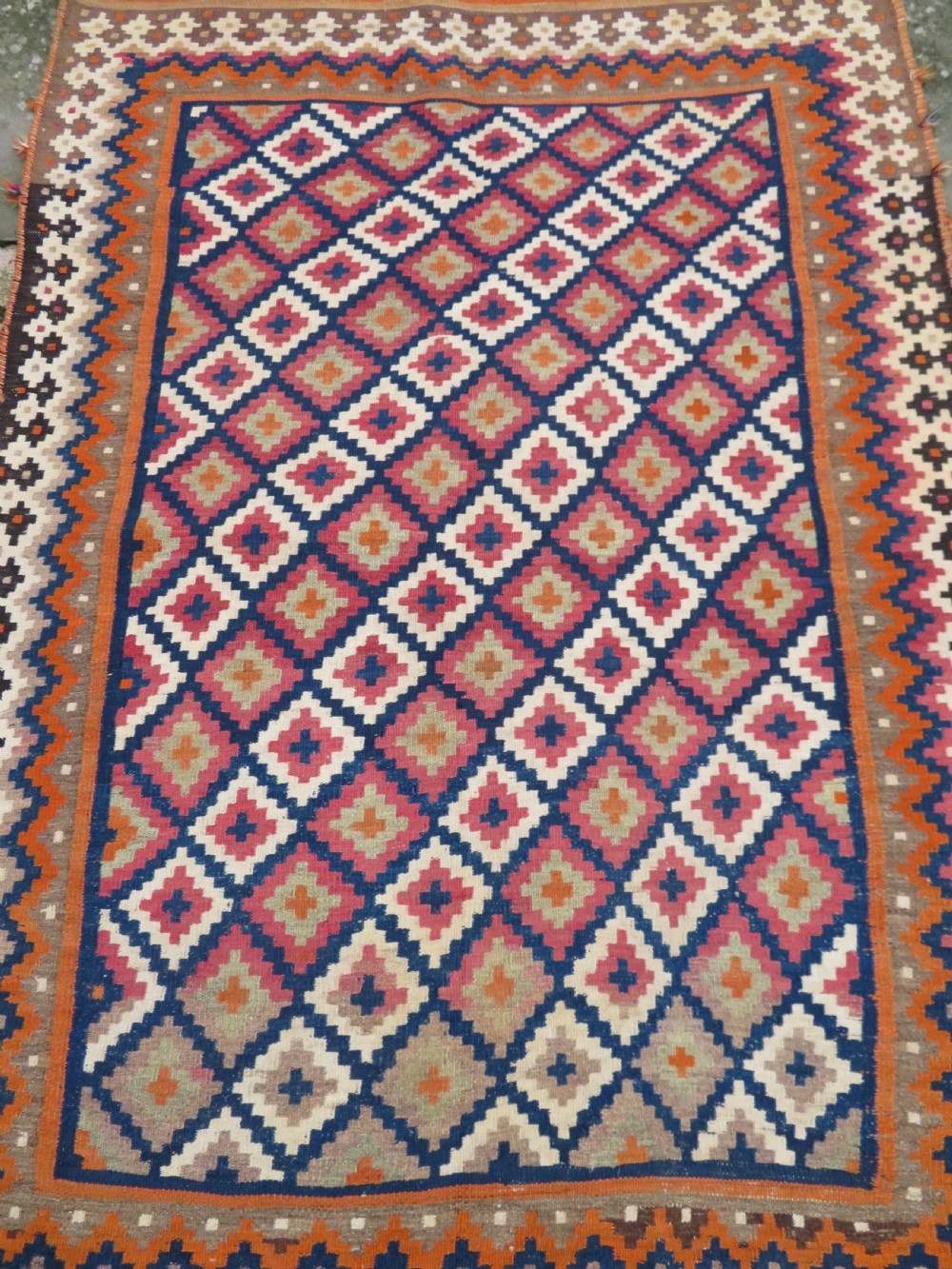 A handwoven Qashqai kilim rug featuring a geometric diamond lattice pattern in terracotta, navy blue, red, and cream with fringed ends. View III