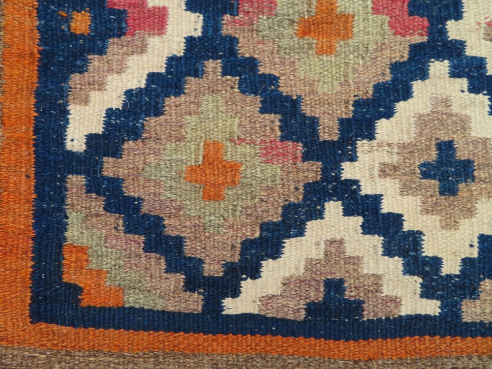 A handwoven Qashqai kilim rug featuring a geometric diamond lattice pattern in terracotta, navy blue, red, and cream with fringed ends. View IV