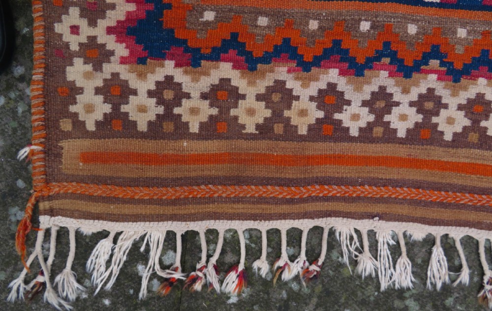A handwoven Qashqai kilim rug featuring a geometric diamond lattice pattern in terracotta, navy blue, red, and cream with fringed ends. View V