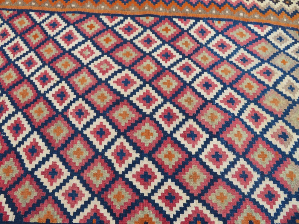 A handwoven Qashqai kilim rug featuring a geometric diamond lattice pattern in terracotta, navy blue, red, and cream with fringed ends. View IX