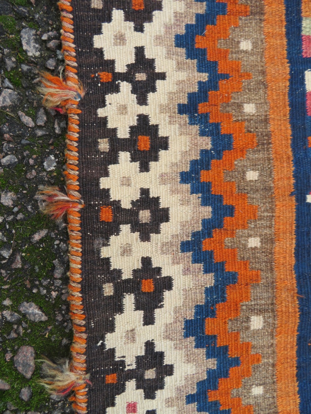 A handwoven Qashqai kilim rug featuring a geometric diamond lattice pattern in terracotta, navy blue, red, and cream with fringed ends. View X