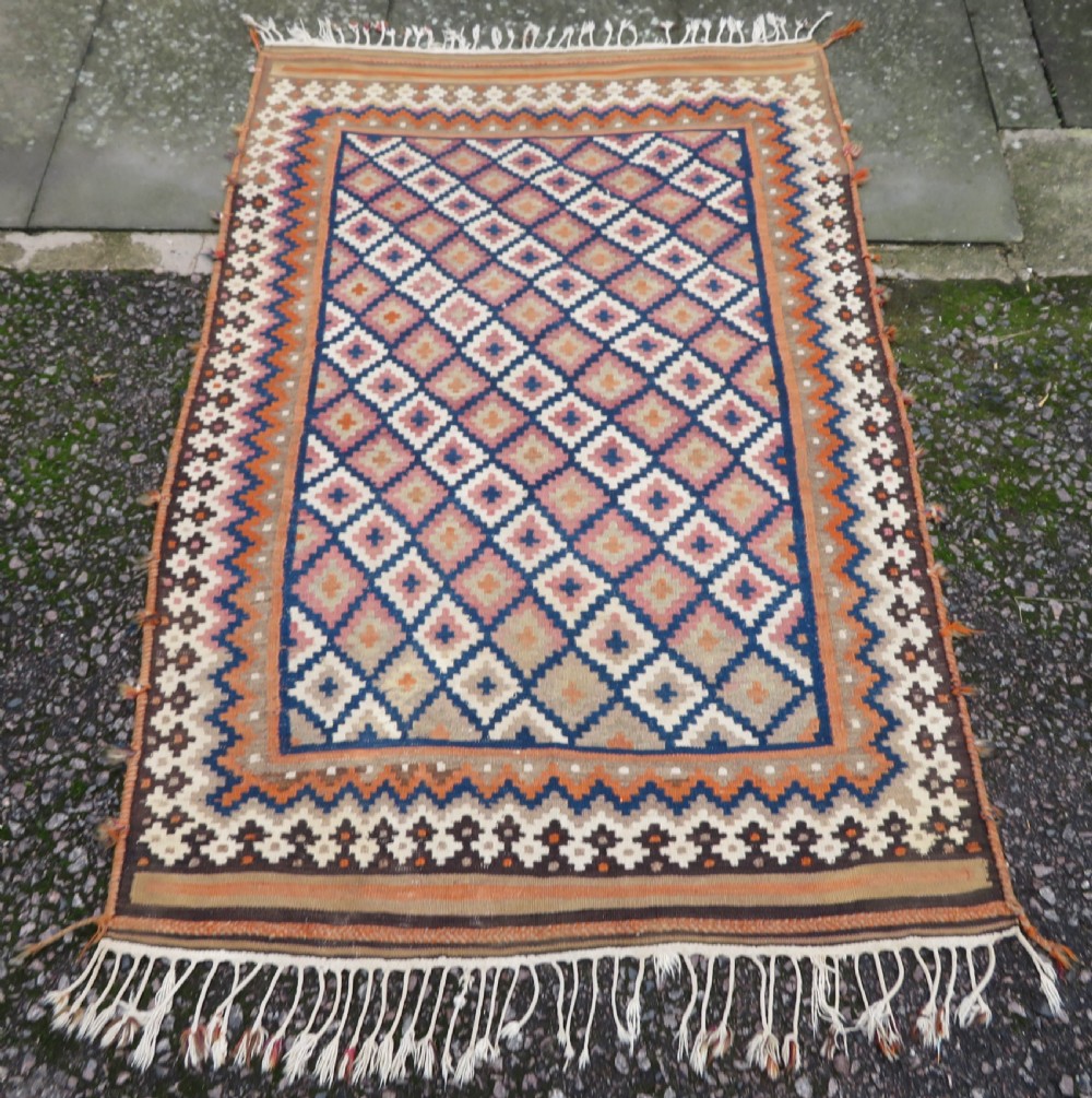 A handwoven Qashqai kilim rug featuring a geometric diamond lattice pattern in terracotta, navy blue, red, and cream with fringed ends. View XI