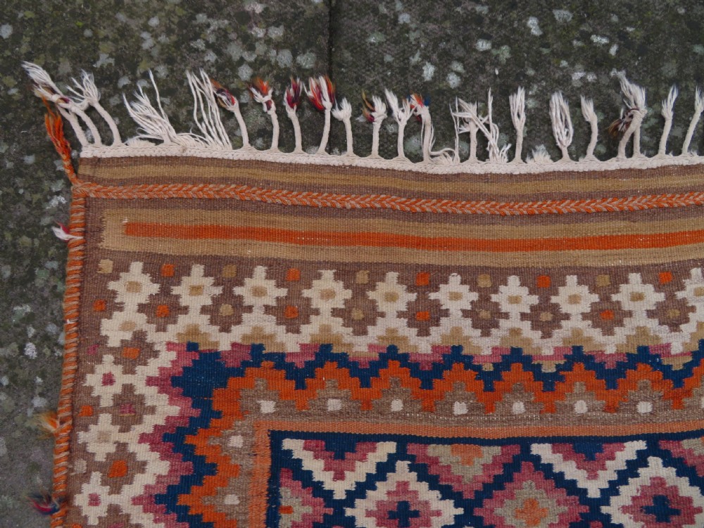 A handwoven Qashqai kilim rug featuring a geometric diamond lattice pattern in terracotta, navy blue, red, and cream with fringed ends. View XVIII