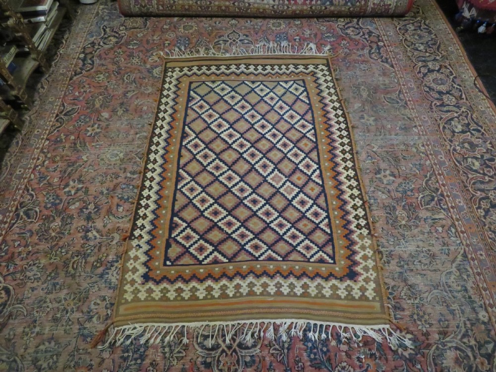 A handwoven Qashqai kilim rug featuring a geometric diamond lattice pattern in terracotta, navy blue, red, and cream with fringed ends. View XX