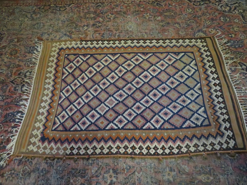 A handwoven Qashqai kilim rug featuring a geometric diamond lattice pattern in terracotta, navy blue, red, and cream with fringed ends. View XXI