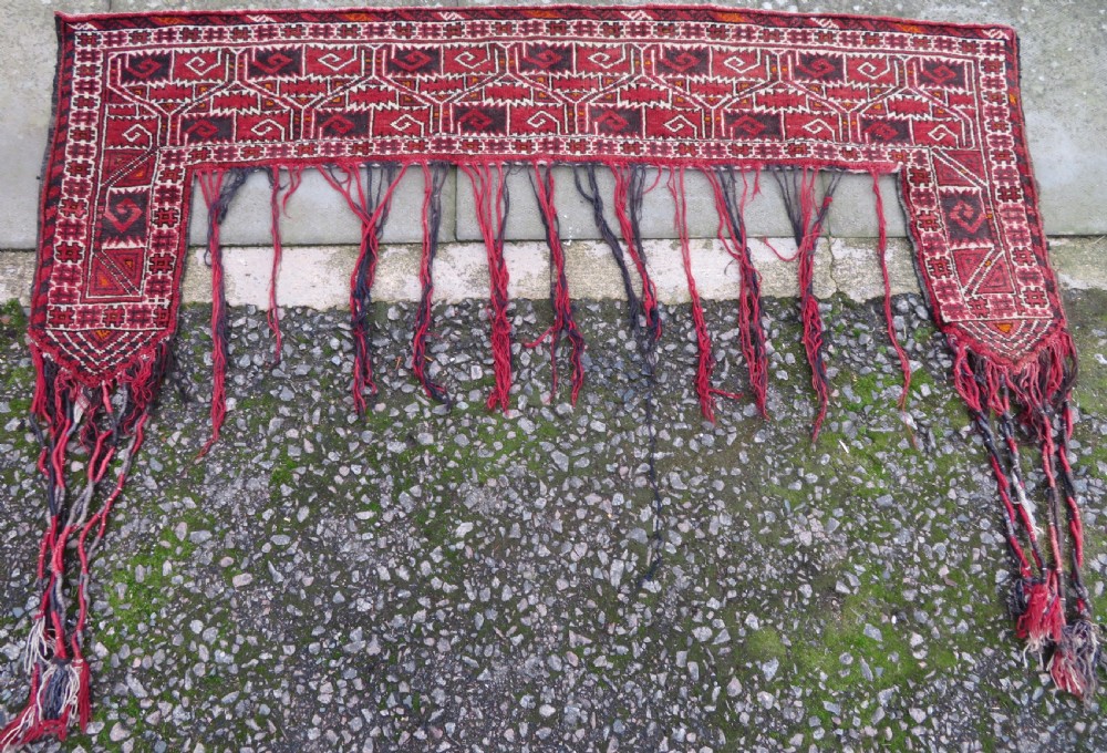 A U-shaped hand-woven Yomut Turkmen kapunuk textile in deep red and dark brown wool with geometric patterns and long hanging tassels along the inner arch.