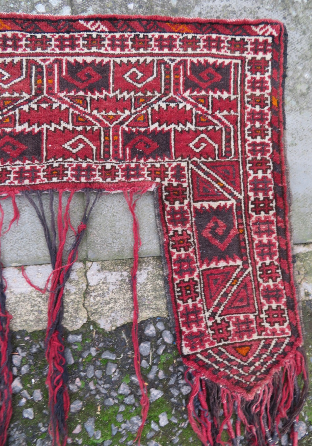 A U-shaped hand-woven Yomut Turkmen kapunuk textile in deep red and dark brown wool with geometric patterns and long hanging tassels along the inner arch. View II