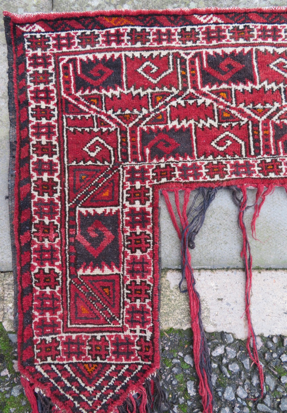 A U-shaped hand-woven Yomut Turkmen kapunuk textile in deep red and dark brown wool with geometric patterns and long hanging tassels along the inner arch. View III