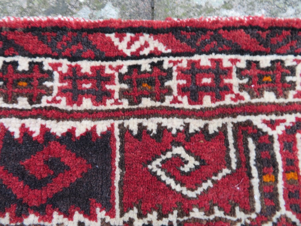 A U-shaped hand-woven Yomut Turkmen kapunuk textile in deep red and dark brown wool with geometric patterns and long hanging tassels along the inner arch. View V