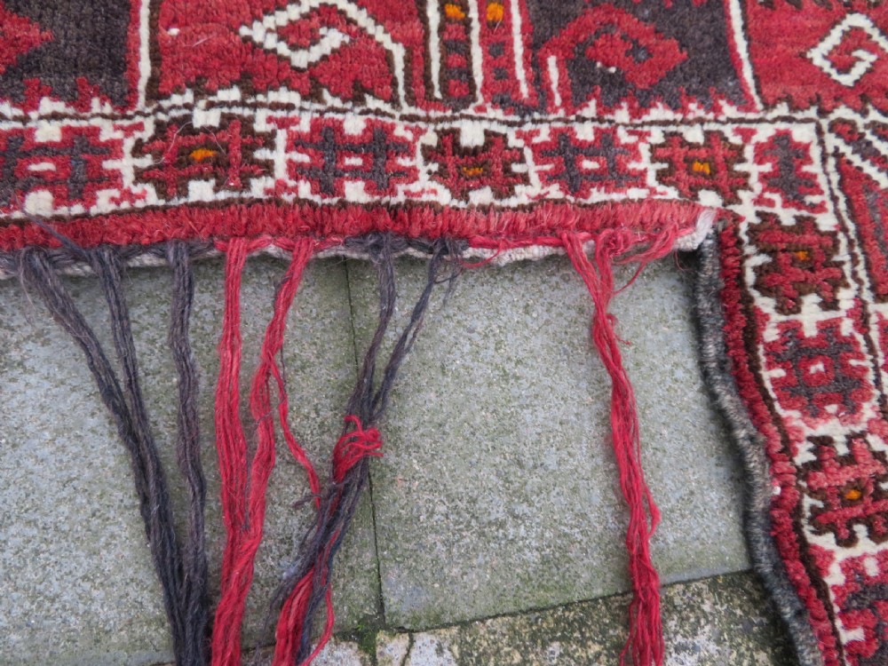 A U-shaped hand-woven Yomut Turkmen kapunuk textile in deep red and dark brown wool with geometric patterns and long hanging tassels along the inner arch. View VII
