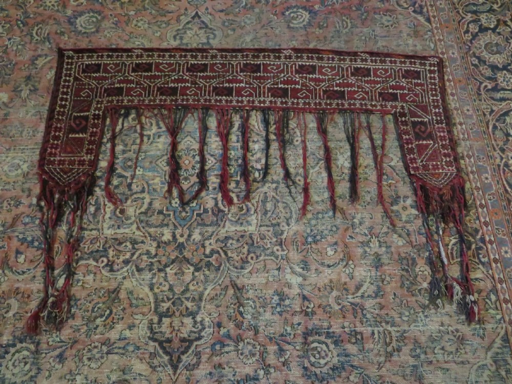 A U-shaped hand-woven Yomut Turkmen kapunuk textile in deep red and dark brown wool with geometric patterns and long hanging tassels along the inner arch. View XVII