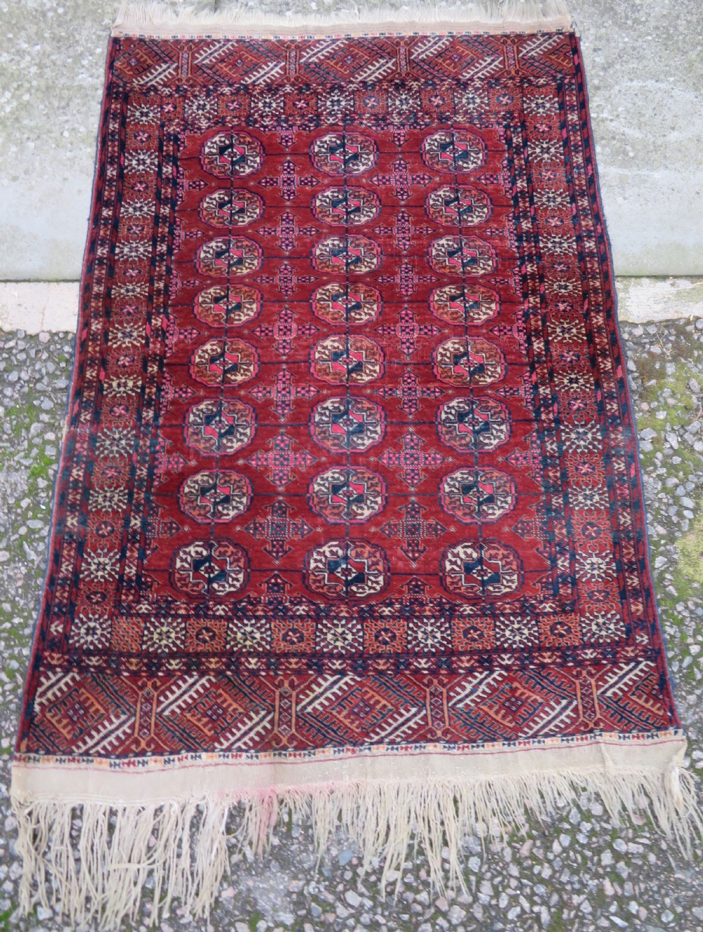 A rectangular hand-knotted Tekke Turkmen wool rug featuring three columns of octagonal gol medallions on a deep red field with geometric borders and fringed ends.