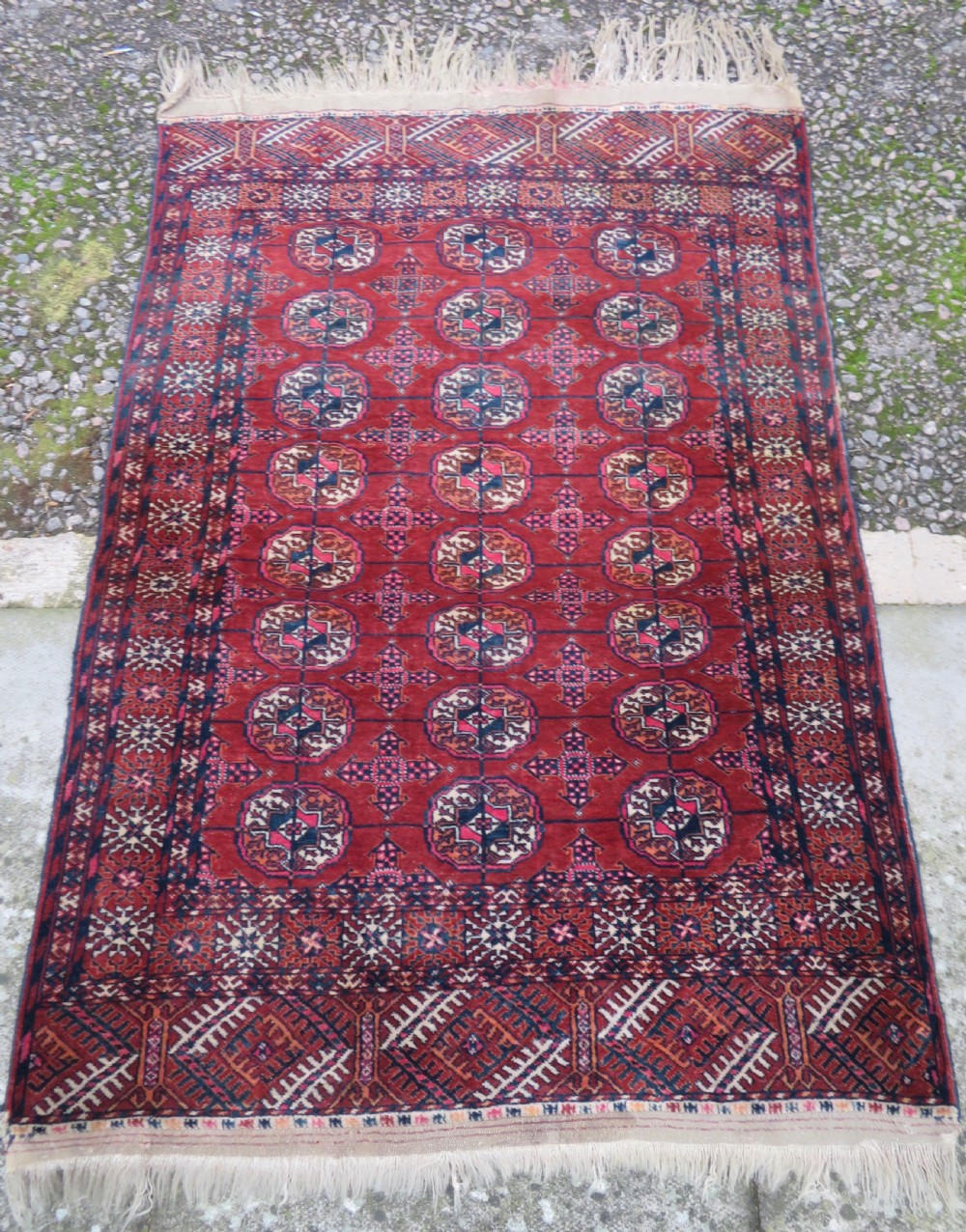 A rectangular hand-knotted Tekke Turkmen wool rug featuring three columns of octagonal gol medallions on a deep red field with geometric borders and fringed ends. View II