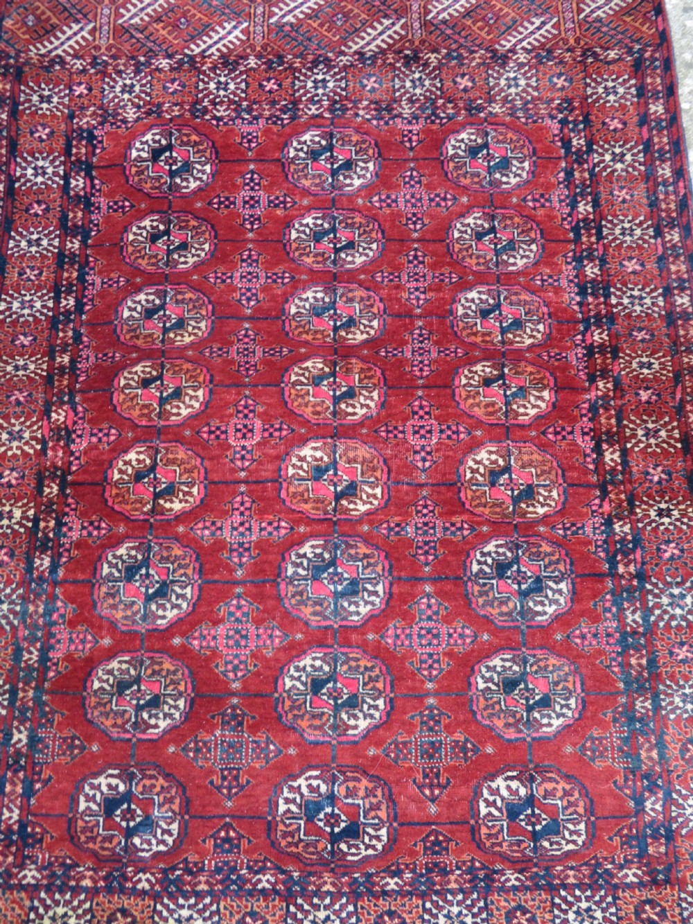 A rectangular hand-knotted Tekke Turkmen wool rug featuring three columns of octagonal gol medallions on a deep red field with geometric borders and fringed ends. View III