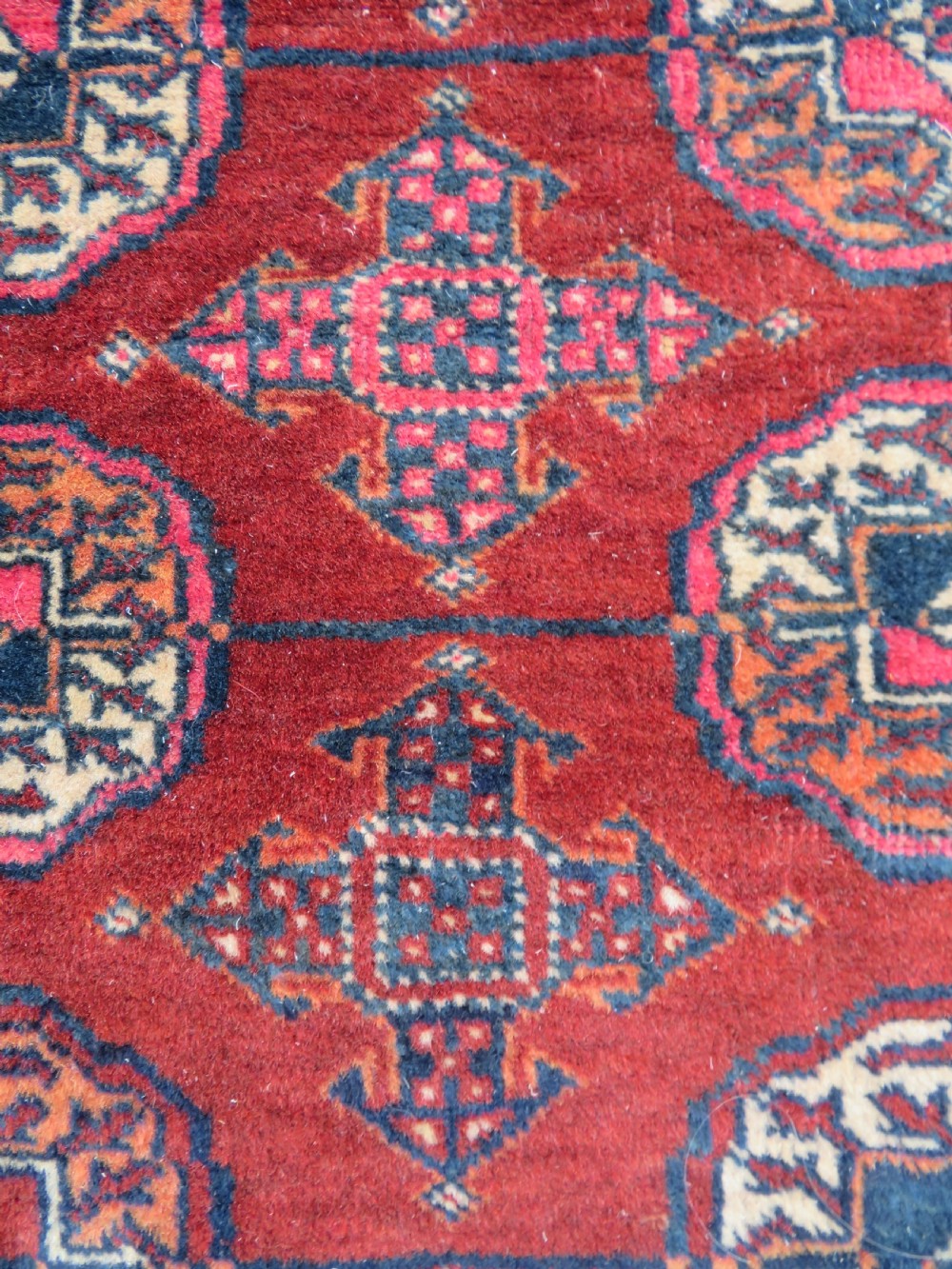 A rectangular hand-knotted Tekke Turkmen wool rug featuring three columns of octagonal gol medallions on a deep red field with geometric borders and fringed ends. View IV