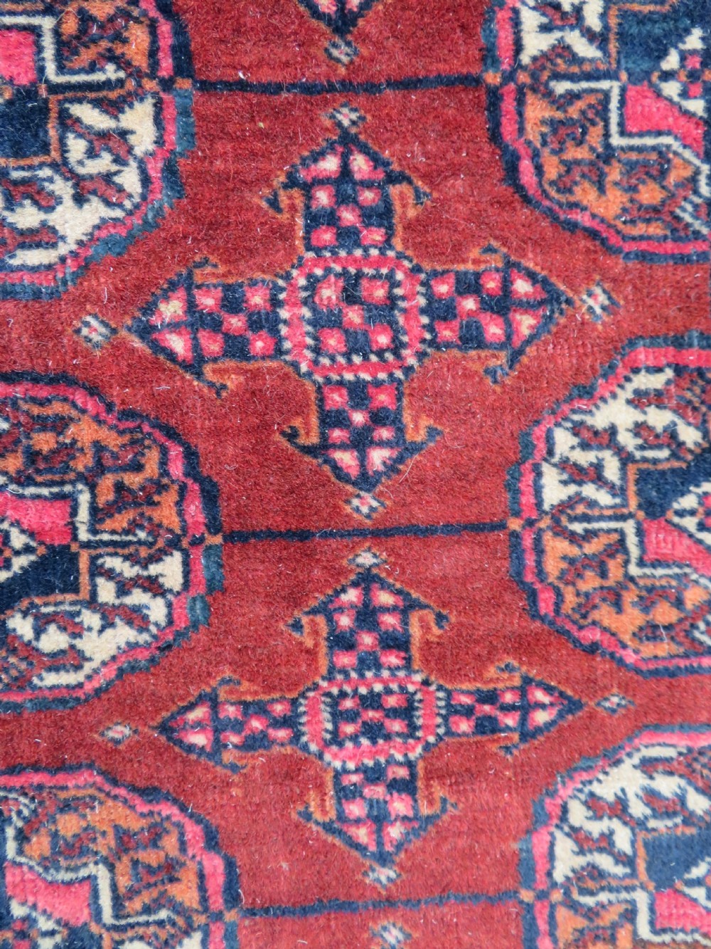 A rectangular hand-knotted Tekke Turkmen wool rug featuring three columns of octagonal gol medallions on a deep red field with geometric borders and fringed ends. View VI