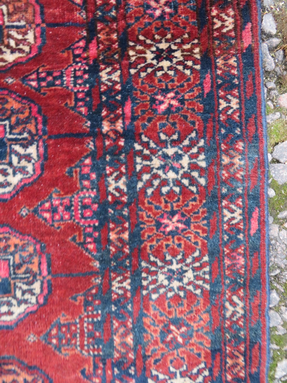 A rectangular hand-knotted Tekke Turkmen wool rug featuring three columns of octagonal gol medallions on a deep red field with geometric borders and fringed ends. View VII