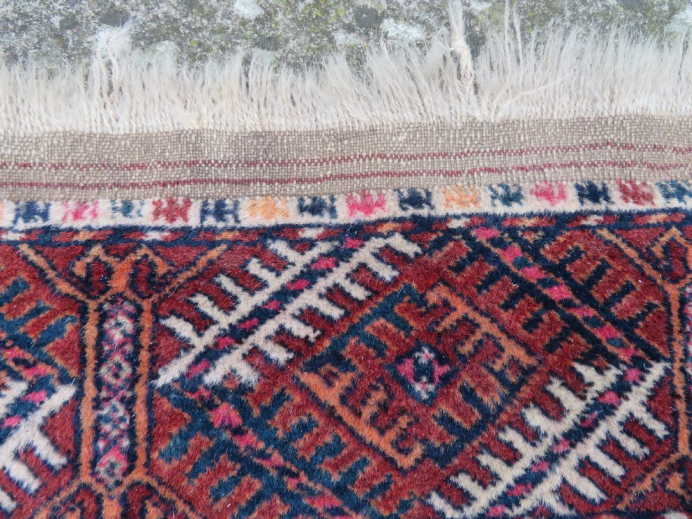 A rectangular hand-knotted Tekke Turkmen wool rug featuring three columns of octagonal gol medallions on a deep red field with geometric borders and fringed ends. View IX