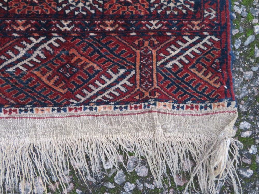 A rectangular hand-knotted Tekke Turkmen wool rug featuring three columns of octagonal gol medallions on a deep red field with geometric borders and fringed ends. View XII