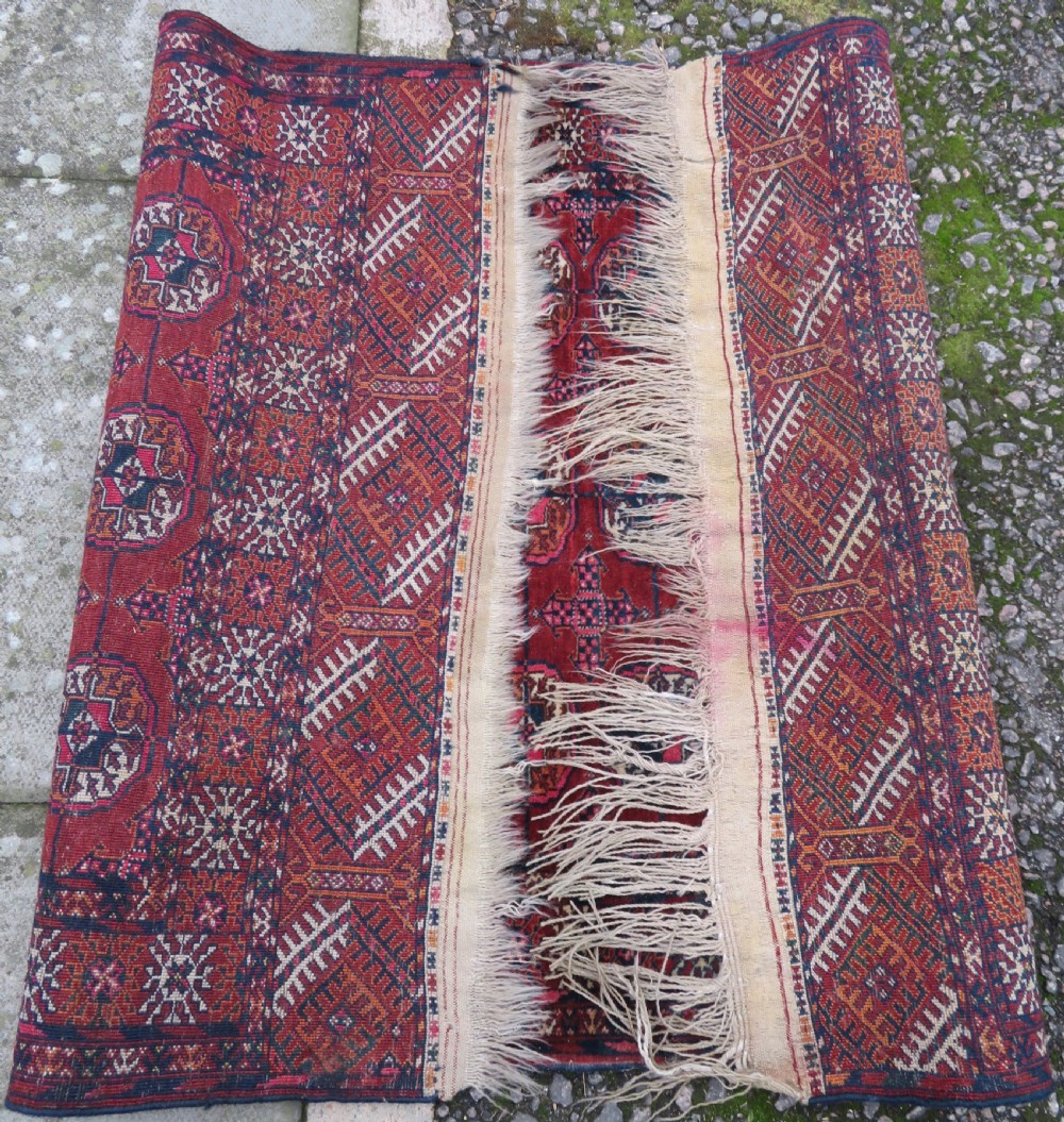 A rectangular hand-knotted Tekke Turkmen wool rug featuring three columns of octagonal gol medallions on a deep red field with geometric borders and fringed ends. View XV