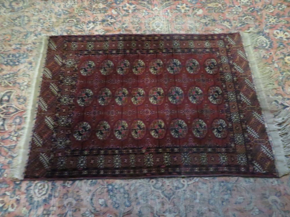 A rectangular hand-knotted Tekke Turkmen wool rug featuring three columns of octagonal gol medallions on a deep red field with geometric borders and fringed ends. View XIX